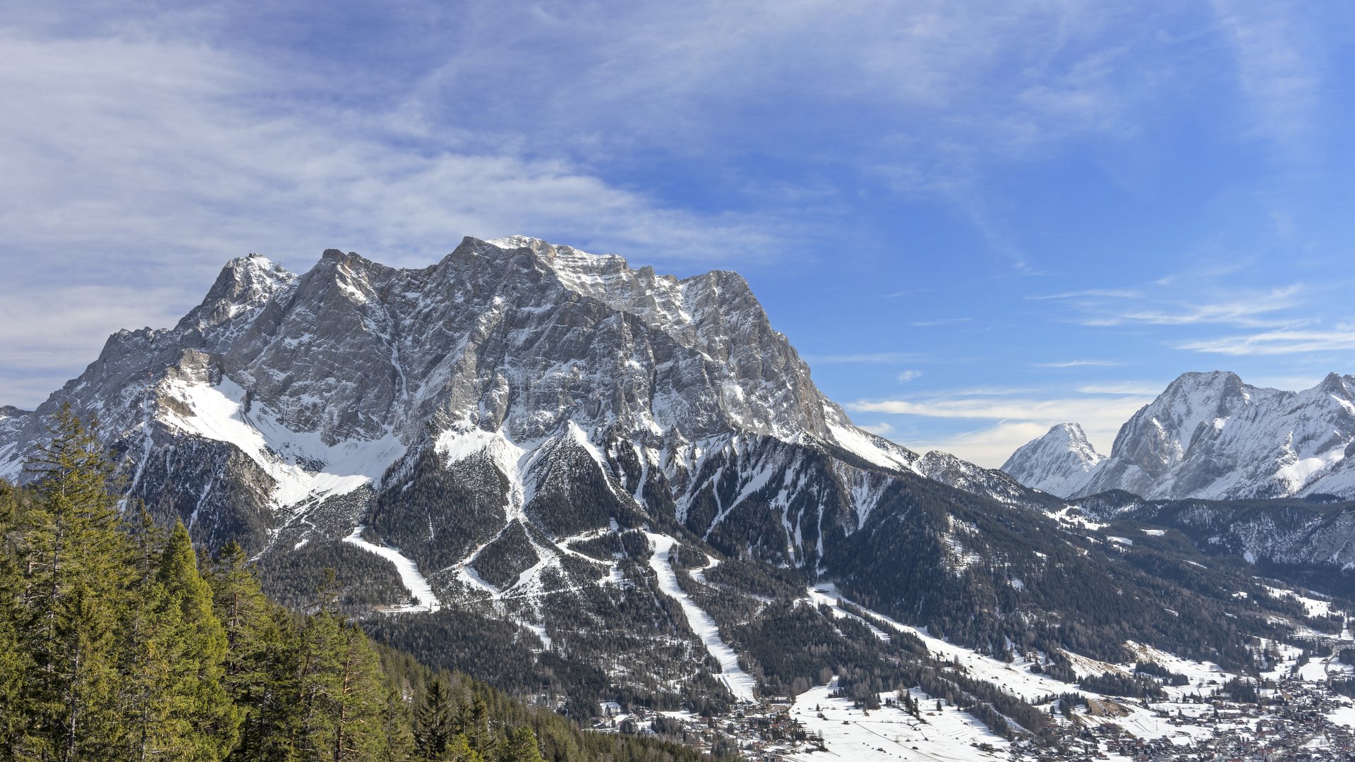 Kultur im Alpenvorland Schneebedeckte Alpen mit Tannenwald und Dorf im Tal unter blauem Himmel